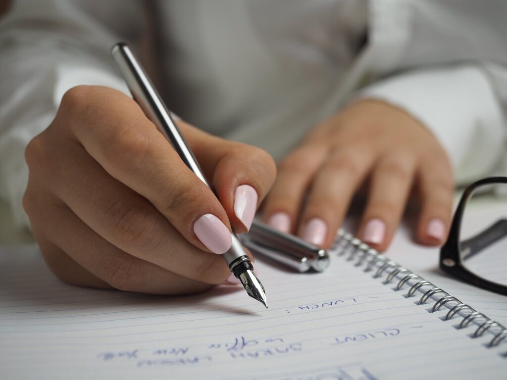 A woman in a white buttoned-up shirt holding a pen as she keeps notes on a notebook.