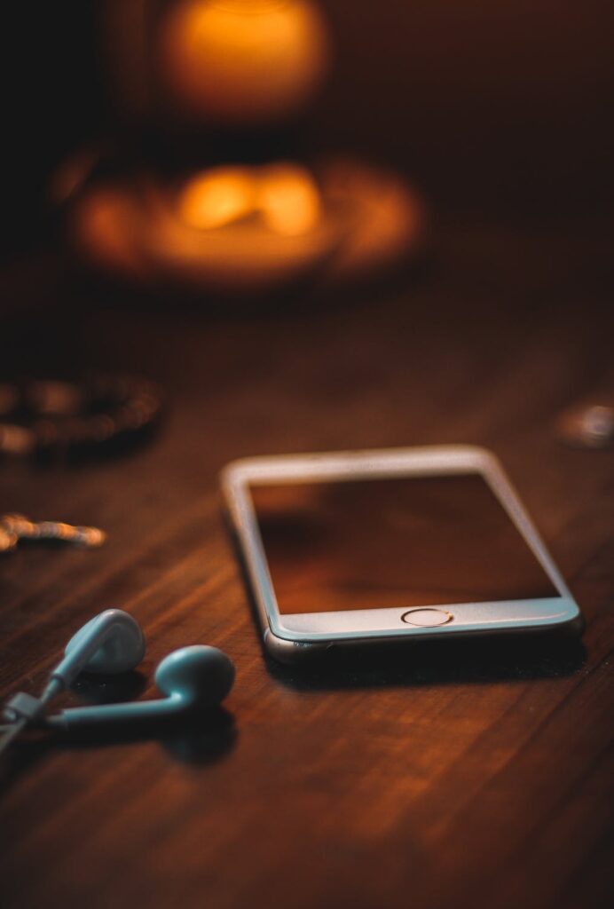 A white smartphone and ear buds on a wooden surface.